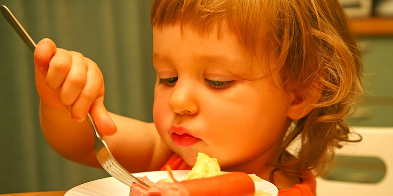 Little girl eating hot dog with a fork