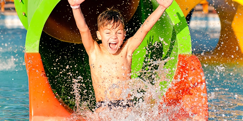young boy sliding down green and orange waterslide
