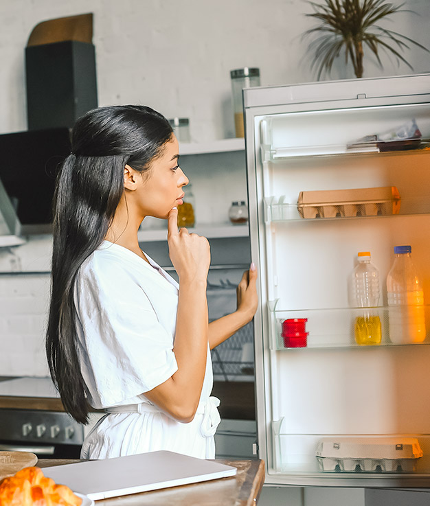 female looking in refrigerator for something to eat with her hand on her chin thinking