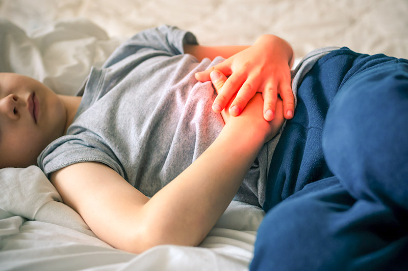 Child laying in bed holding stomach in pain