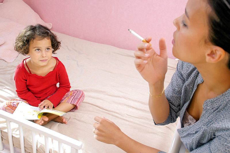 young girl and mom in bedroom. Mom is smoking cigarette.