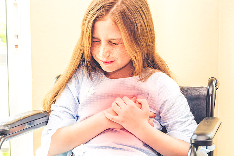 young girl sitting in wheelchair grabbing her chest in pain