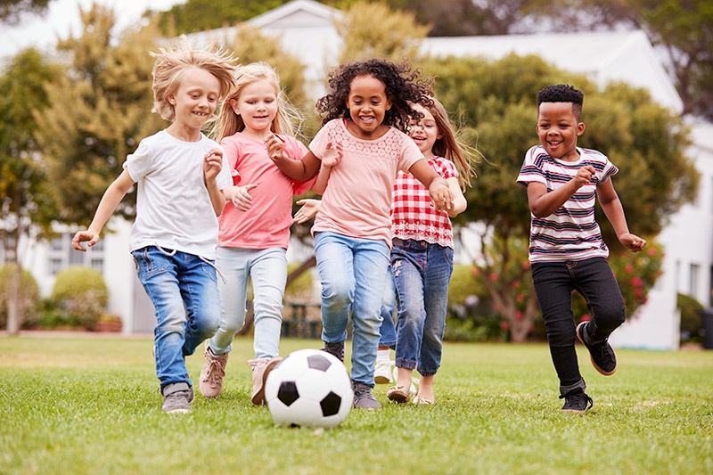 Group of young children running outside playing soccer together