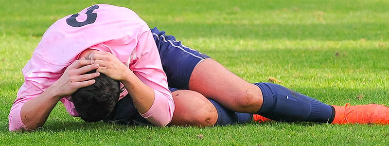 Soccer player laying on field holding head because of injury