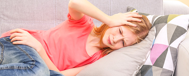 young girl lying on couch with a bad headache holding hand to her forehead