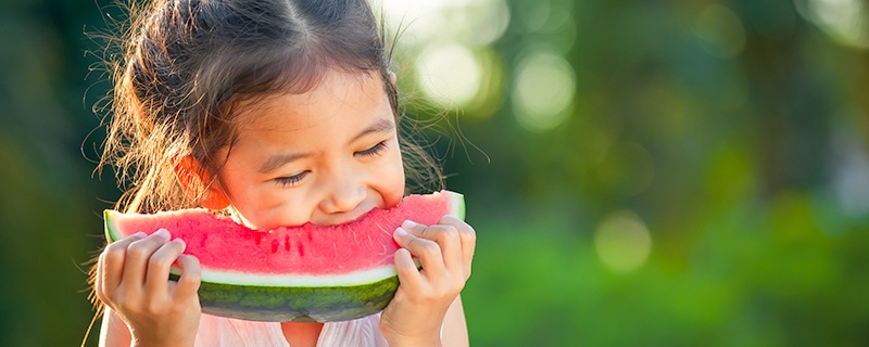 young girl eating a slice of watermelon outside