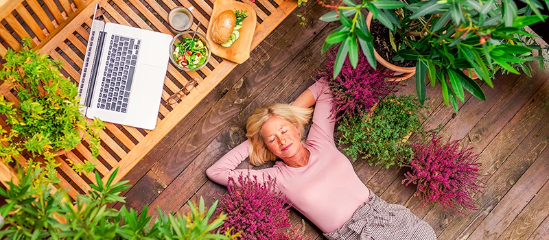 woman relaxing on front porch, laying with eyes closed and hands behind her head with healthy food options, sandwich and salad sitting on bench above her head