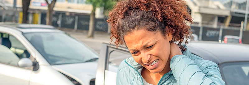 woman standing outside car after a car accident rubbing her neck from pain