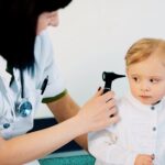 A woman is closely examining a child's ear with a microphone, assessing for any potential issues
