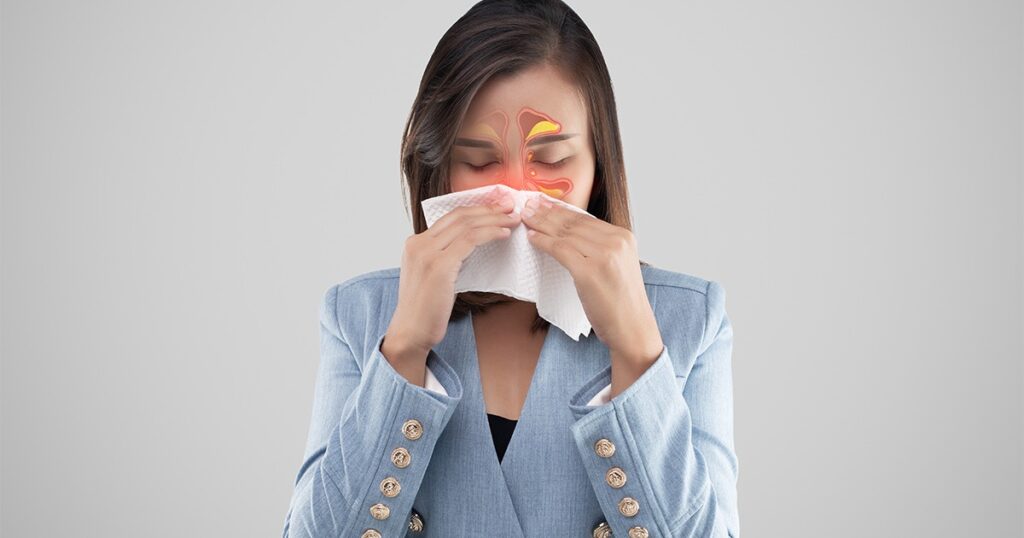 A woman blowing her nose with a tissue, showing symptoms of a sinus infection contagious illness.