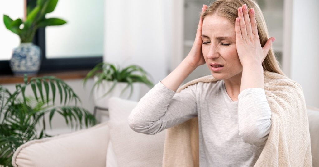 A woman on a couch, hands on her head, displaying signs of mild concussion.
