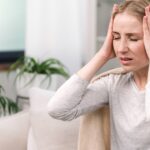 A woman on a couch, hands on her head, displaying signs of mild concussion.