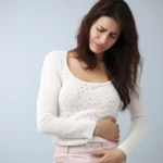 Woman holding her lower abdomen while appearing visibly uncomfortable.