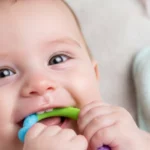 Baby with a teething ring, showing signs of teething and runny nose.