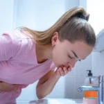 Woman leaning over bathroom sink, feeling nauseous.