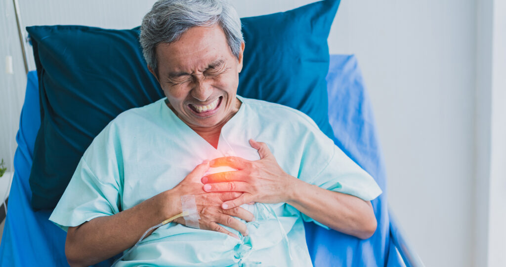 Elderly man in hospital bed clutching his chest in pain.