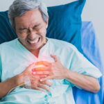 Elderly man in hospital bed clutching his chest in pain.