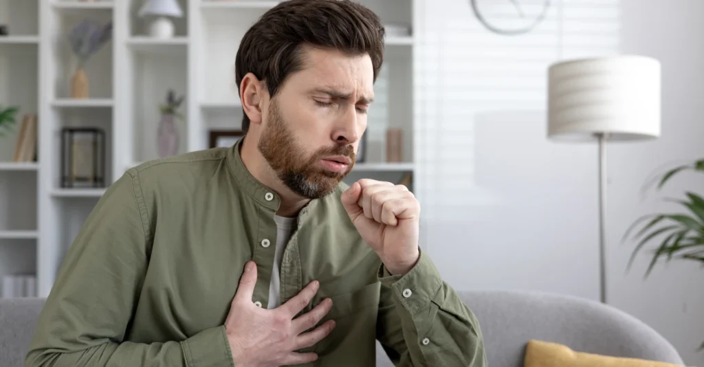 Man coughing into his fist while holding his hand to his chest.