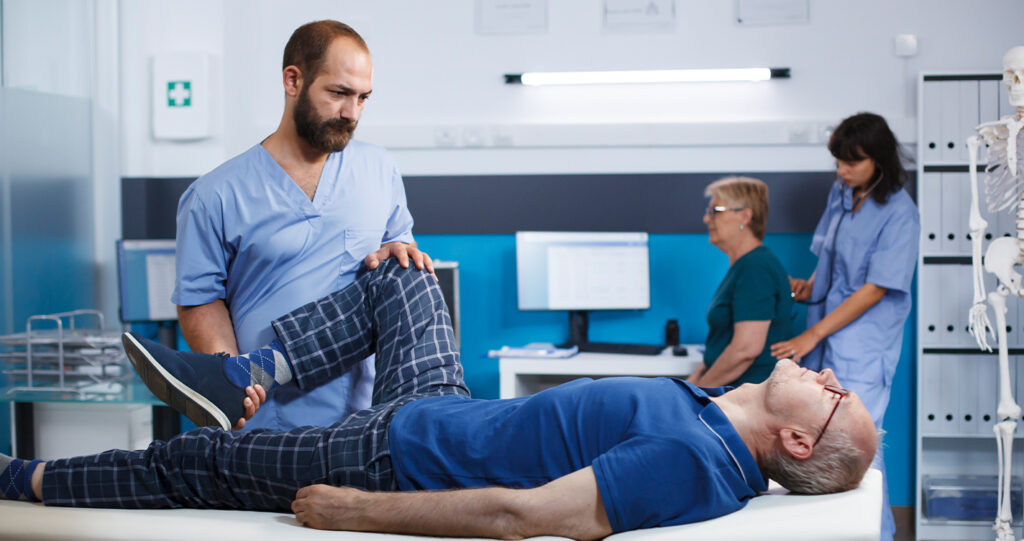 Physical therapist guiding an elderly man through a leg stretch.