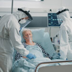 Medical staff in full protective gear treating an elderly patient wearing an oxygen mask.