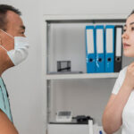 A patient describes throat discomfort to a healthcare professional wearing a medical mask.