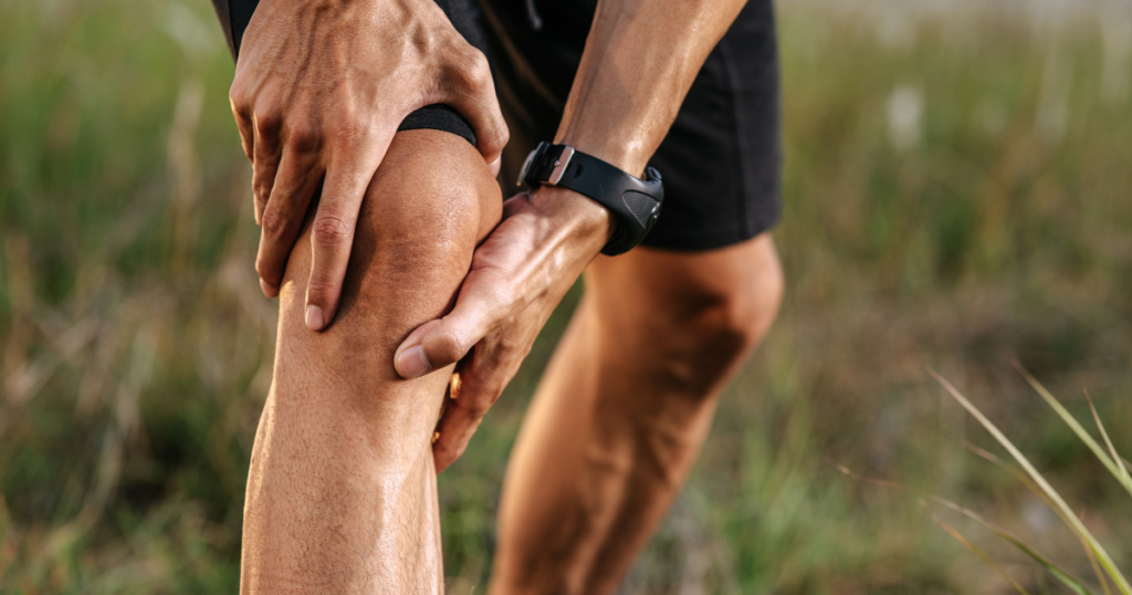 Man holding his knee outdoors, showing knee pain.
