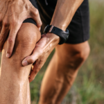 Man holding his knee outdoors, showing knee pain.