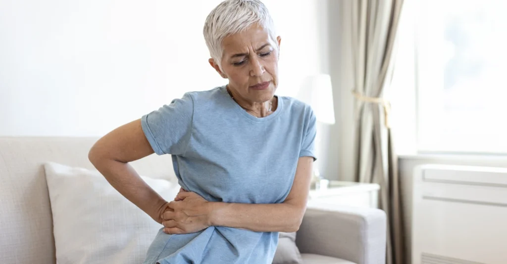 Woman with a pained expression holding her side and lower back on a sofa.