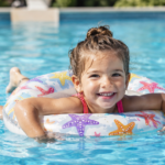Smiling girl floating on a pool ring in clear blue water.