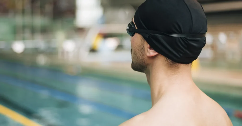 Swimmer in a black cap and goggles looking out at an indoor pool.