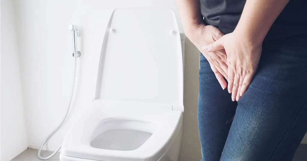 Woman experiencing urinary discomfort while standing beside a toilet.