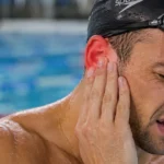 Male swimmer holding a painful, red ear beside a swimming pool.
