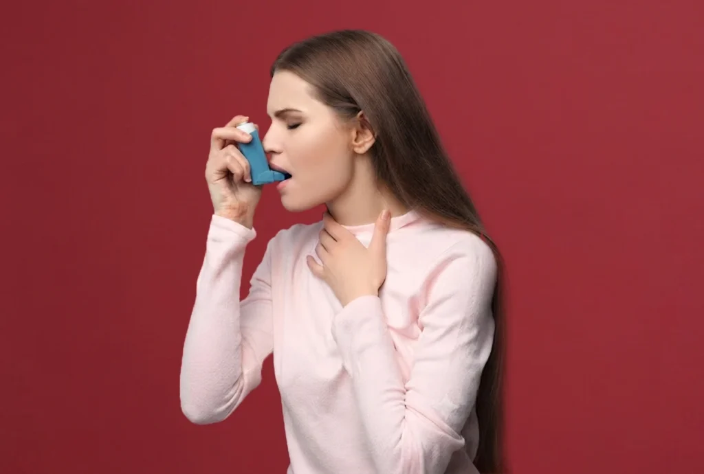 Woman using a blue inhaler against a red background.