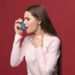Woman using a blue inhaler against a red background.