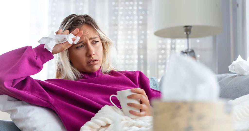 Sick woman resting with tissues and a warm drink.