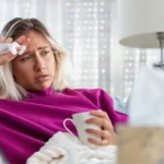 Sick woman resting with tissues and a warm drink.