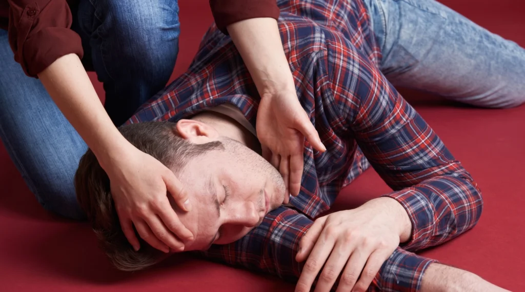 A person placing their hand on the head of another individual lying on the red floor.