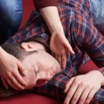 A person placing their hand on the head of another individual lying on the red floor.