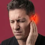 A man grimacing in pain while holding his ear, which is highlighted with a red glow to suggest ear discomfort.