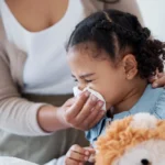 Mother helping her young daughter blow her nose with a tissue.