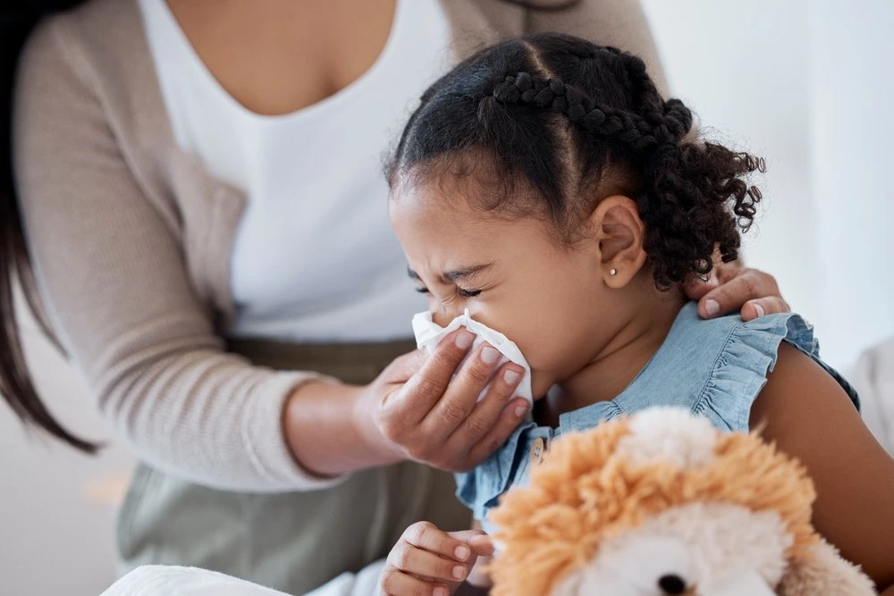 Mother helping her young daughter blow her nose with a tissue.