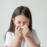 A young girl blowing her nose with a tissue.