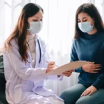 Doctor wearing a mask taking medical notes during patient consultation.
