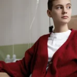 Patient in red cardigan receiving IV treatment in clinic chair.