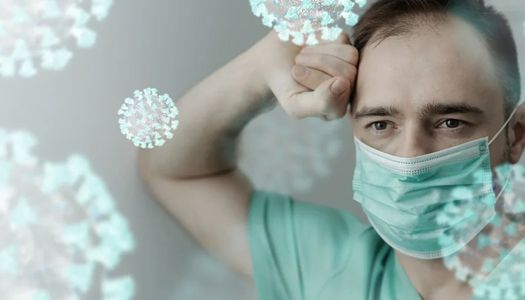 Exhausted medical worker wearing face mask with viral particles floating.