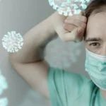 Exhausted medical worker wearing face mask with viral particles floating.