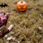 Bloody hand reaching toward glowing jack-o'-lantern in grass setting.