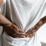 Close-up of a man holding his lower back in pain.